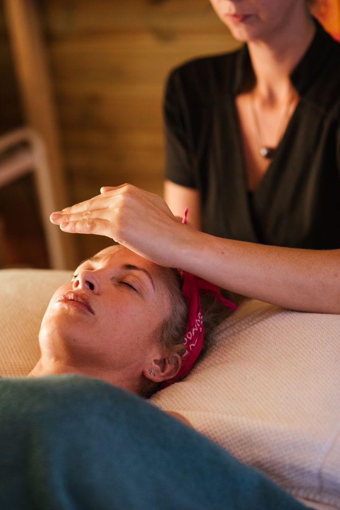 services-03 Relaxed woman with closed eyes lying under blanket while getting reiki therapy treatment from unrecognizable therapist in cozy salon with blurred background