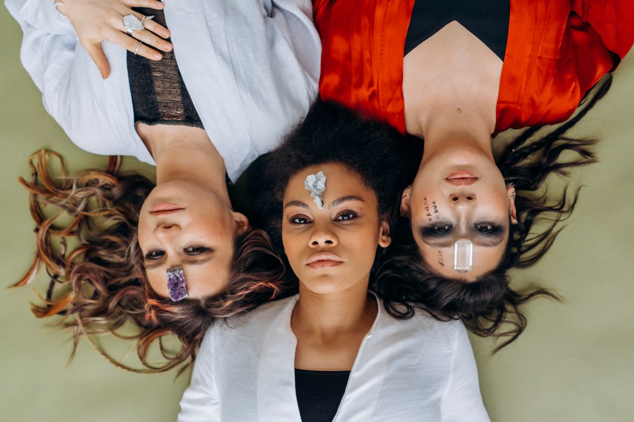 about-us Three diverse women lying together with crystals on foreheads for meditation and relaxation.